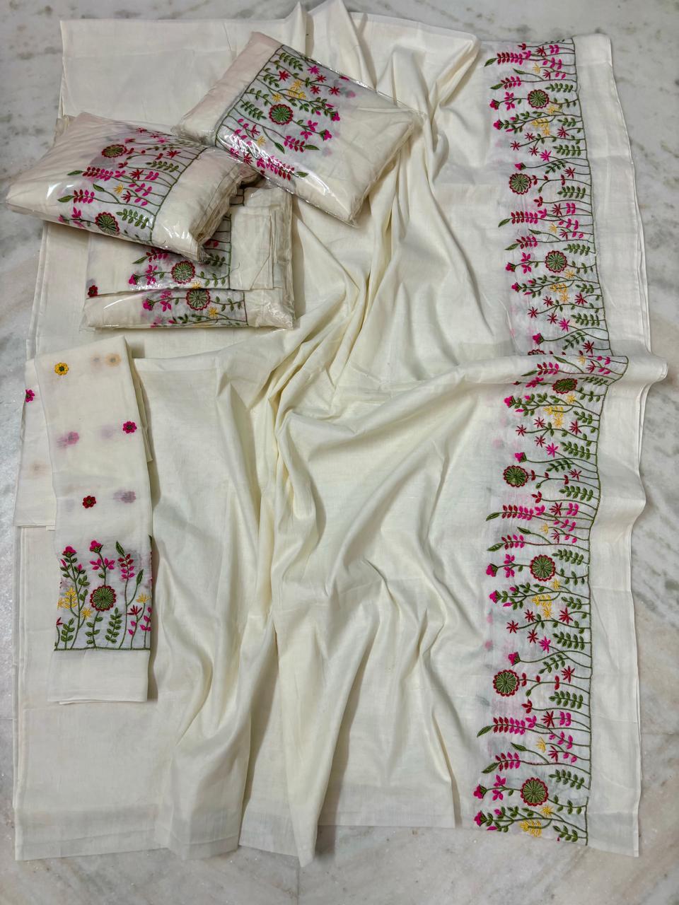 An off-white or cream-colored saree set, featuring detailed floral embroidery in pink, green, and yellow along the borders and on matching fabric pieces.