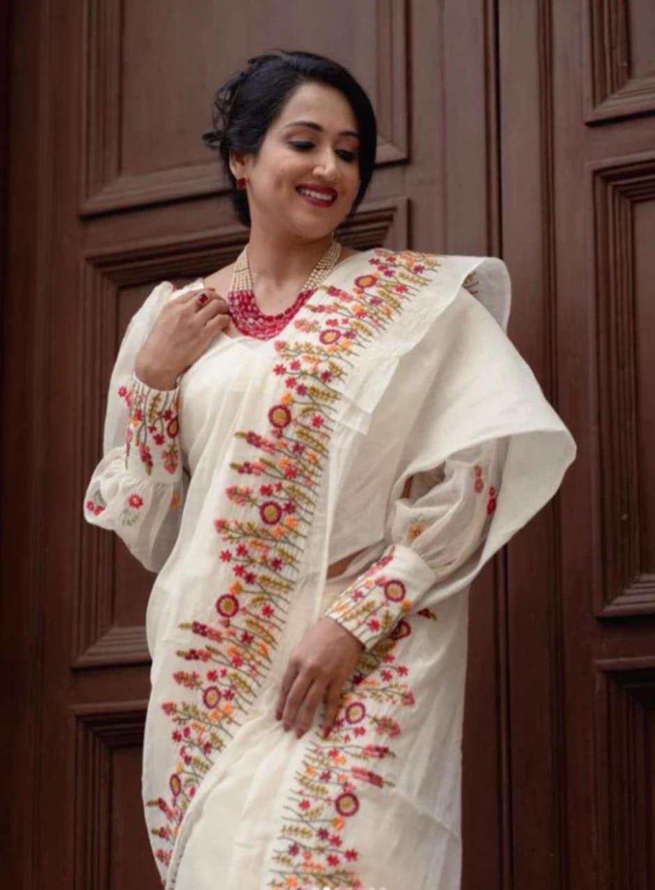 Woman wearing an ivory cotton saree with red and orange floral embroidery on the border and pallu
